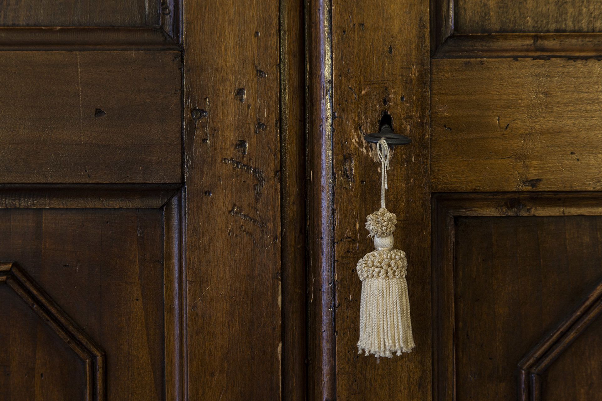 A wooden door with a brass doorknob and a white tassel hanging from it.