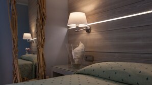 Une chambre d’hôtel avec une tête de lit en bois, une table de chevet avec une lampe, un vase en verre contenant un coquillage et un lit avec une literie à motifs.