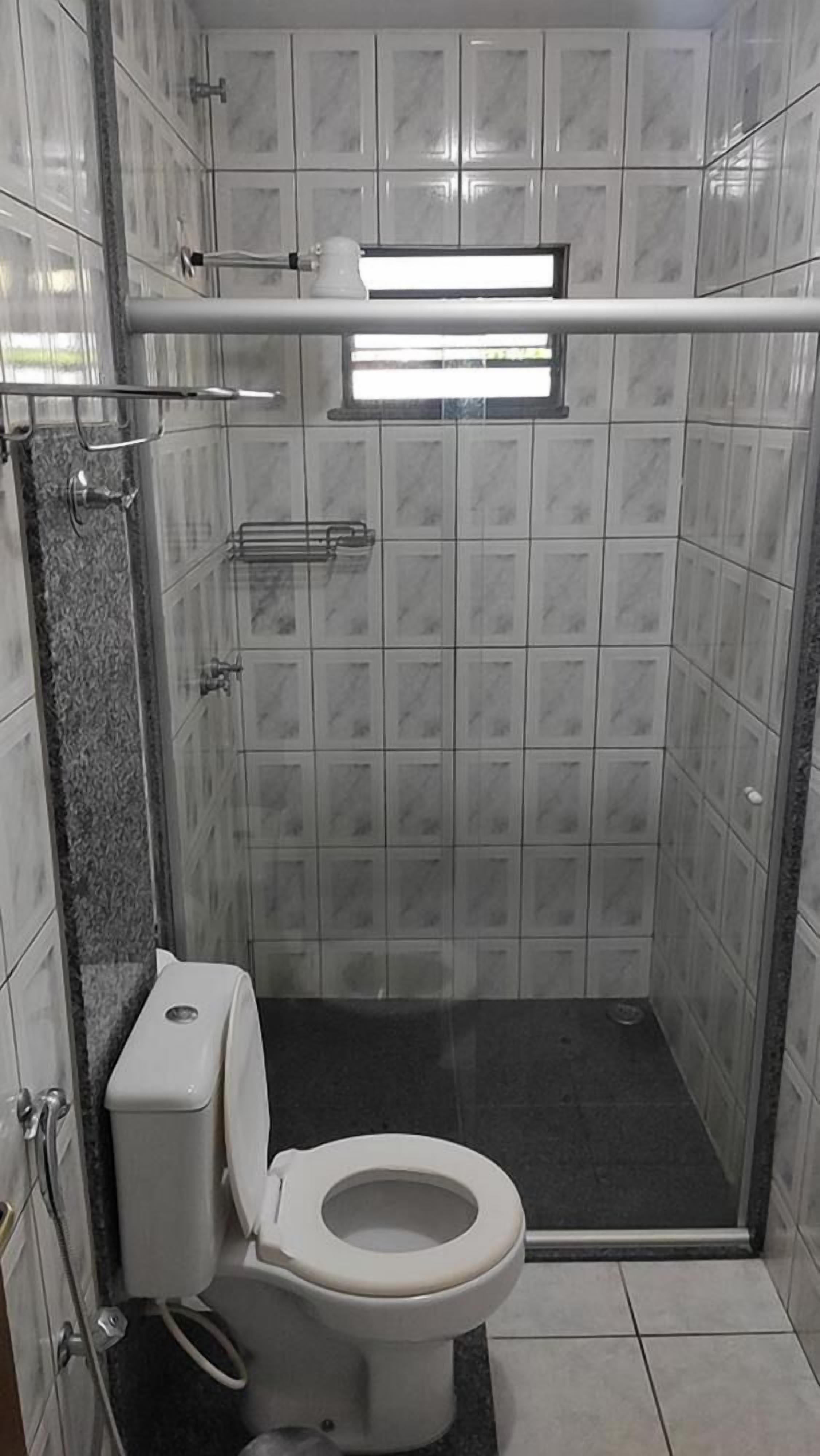 A small, enclosed shower stall with a toilet and a towel rack.