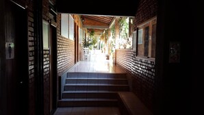 A corridor with brick walls, a tiled floor, and a staircase leading to a bright area with outdoor seating. - Pousada Barcelos (São Roque de Minas)