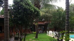 A pathway leading to a building with a tiled roof, surrounded by lush greenery and palm trees. - Pousada Barcelos (São Roque de Minas)