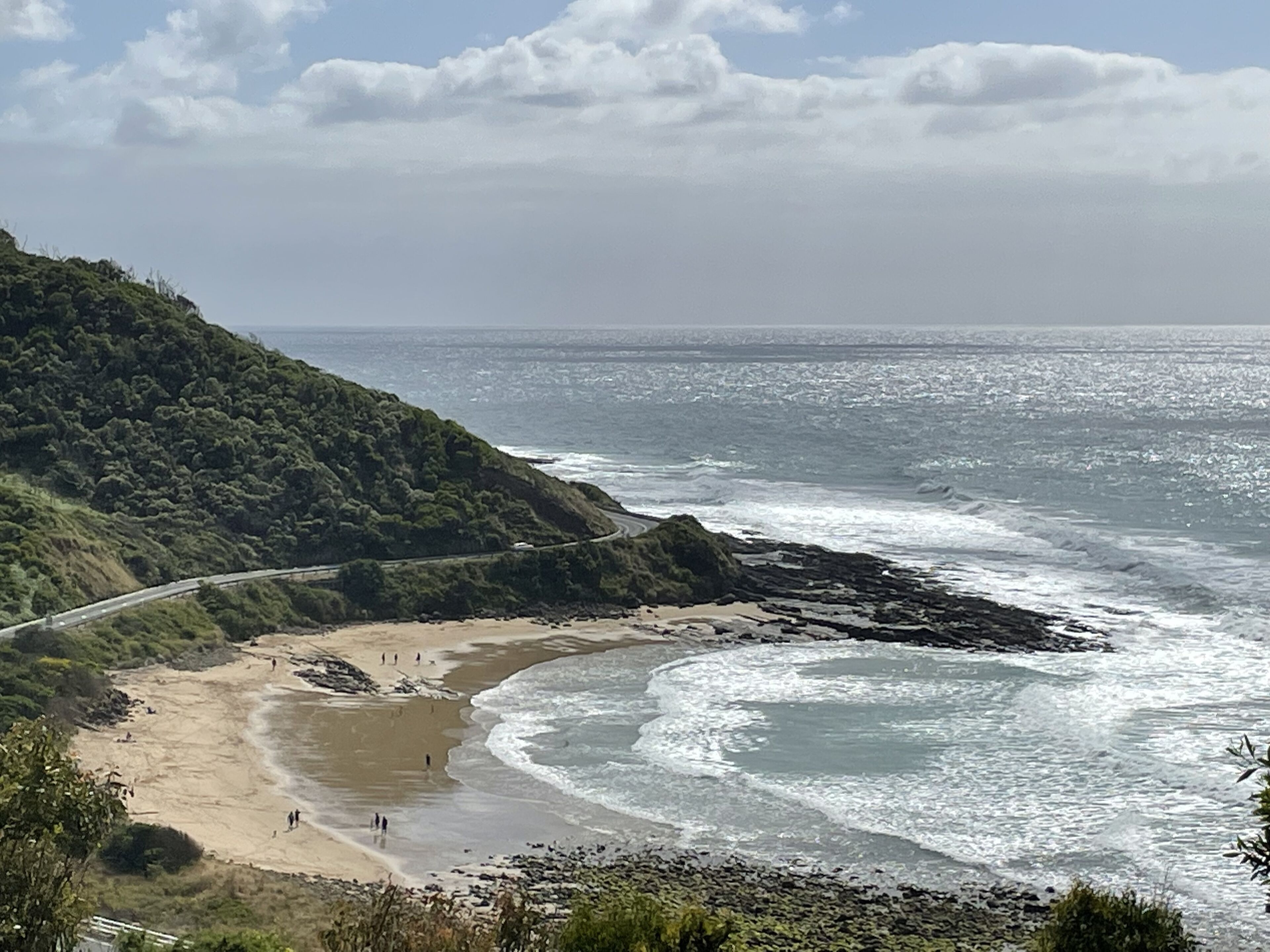 Eine Küstenlandschaft mit einer kurvenreichen Straße, Strand und felsiger Küste.