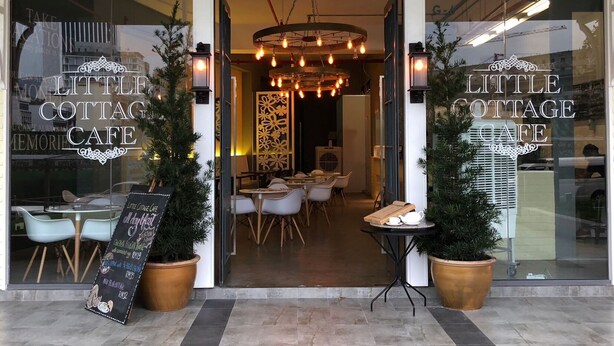 The entrance of Little Cottage Cafe with a modern interior visible through the doorway, featuring a central light fixture and seating area.