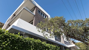 A modern building with a prominent white facade, a brick section, and a large tree in the foreground.