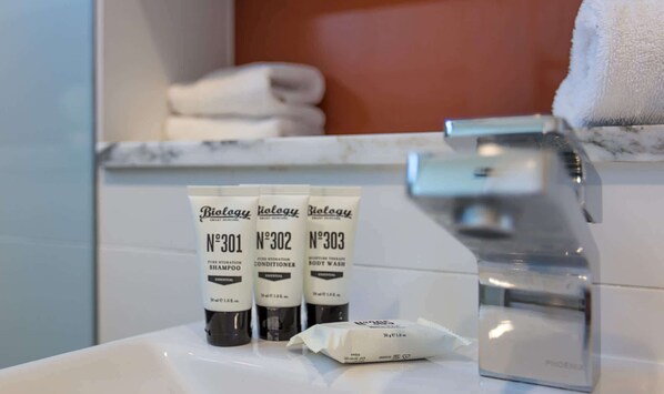 A bathroom with a white sink, two bottles of Biolgy shampoo, a body wash, and a towel on the counter.