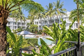Un resort con piscina, palmeras y un edificio blanco con balcones.