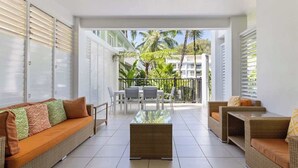 Ein moderner Innenraum mit einer Couch, Sesseln und einem Couchtisch. Ein Balkon bietet Blick auf Palmen und Gebäude.