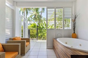 Un balcone con vista su palme, una vasca da bagno bianca e mobili in vimini.