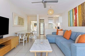 Una sala de estar moderna con sofá, mesa de centro, televisor y comedor.