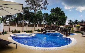 Une piscine avec un pont, entourée de palmiers et d’une clôture en bois.