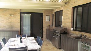 An outdoor kitchen area with a grill, dining table set for four, and a refrigerator. - IDEAL FAMILY BEACH GETAWAY, 1 HR FROM SYDNEY!!! (Umina Beach)