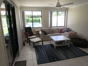 Salón con sofá, sillón, mesa de centro y vistas a una piscina a través de amplios ventanales.