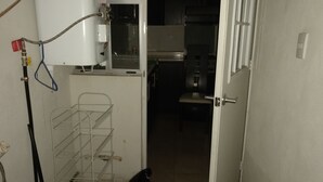 Una cocina con calentador de agua, una estantería metálica y una puerta que da a otra habitación.