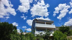 Un edificio de dos pisos con balcones, rodeado de vegetación bajo un cielo azul despejado con nubes dispersas.