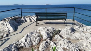 Un banco sobre una plataforma rocosa junto al mar, con barandilla, con vistas al océano.