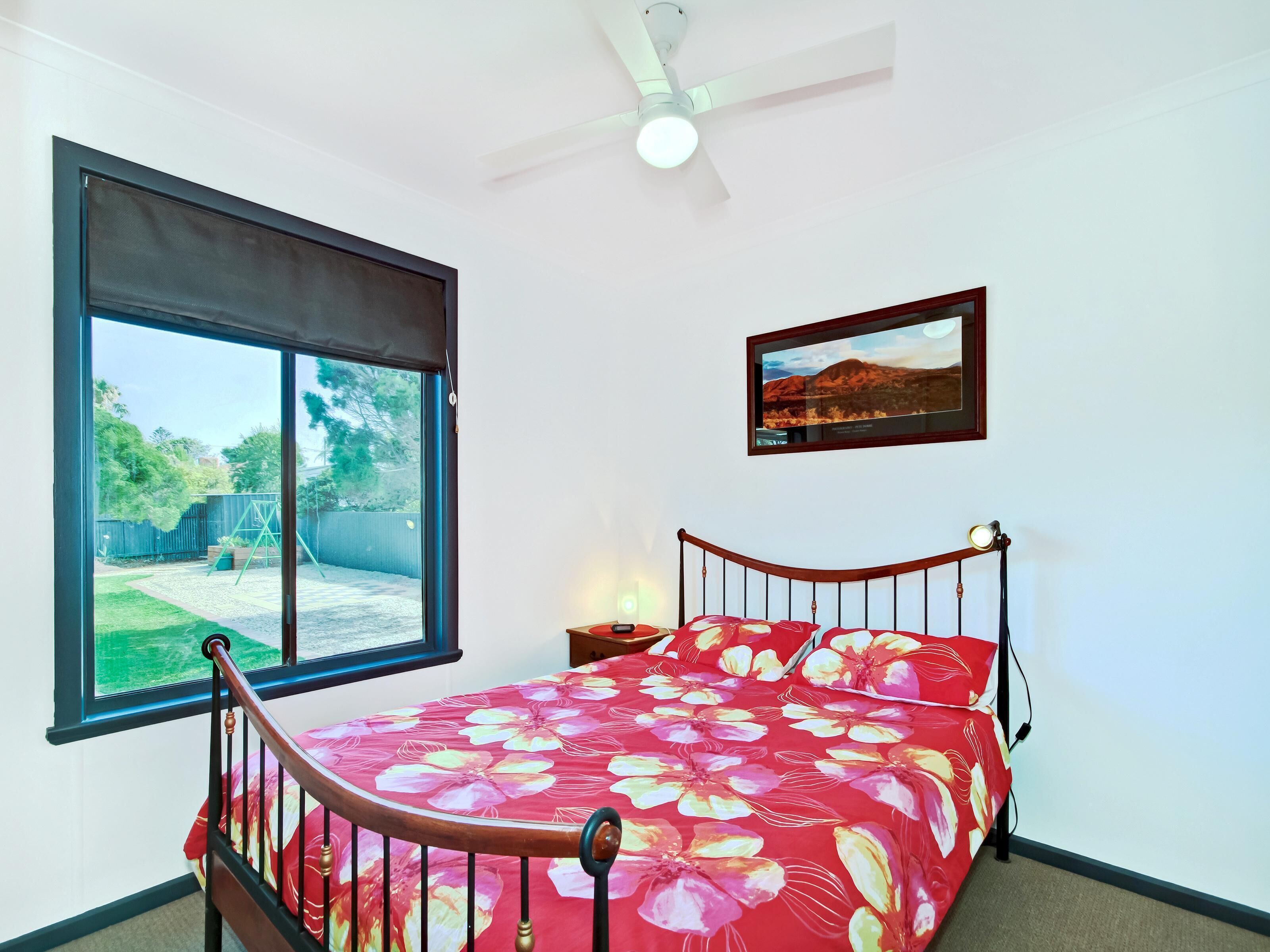 A bedroom with a bed, a window, a ceiling fan, and a framed picture on the wall.