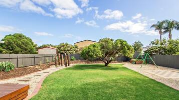 A backyard with a wooden deck, a swing set, and a fenced area.