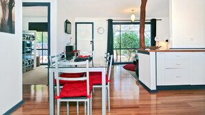 Una cocina moderna con armarios blancos, una isla de madera y un comedor con mesa de vidrio y cojines rojos.