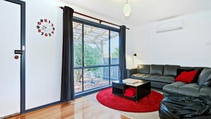 Una sala moderna con un sofá de cuero negro, un tapete rojo y piso de madera.