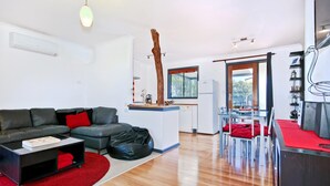 Una sala de estar moderna con un sofá gris, cojines rojos, un sillón de girable negro y una alfombra roja. Se ve una zona de cocina con una mesa y sillas en el fondo.