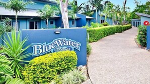 A BlueWater Views hotel entrance with a clear pathway leading to the building, surrounded by lush greenery and palm trees. - Blue water Views 15, Beautiful Apartment on Hamilton Island (Hamilton Island)