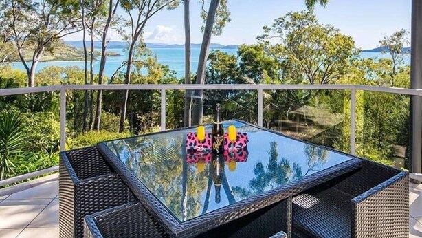 A glass-top table with wicker chairs on a balcony overlooking a coastal landscape. - Blue water Views 15, Beautiful Apartment on Hamilton Island (Hamilton Island)