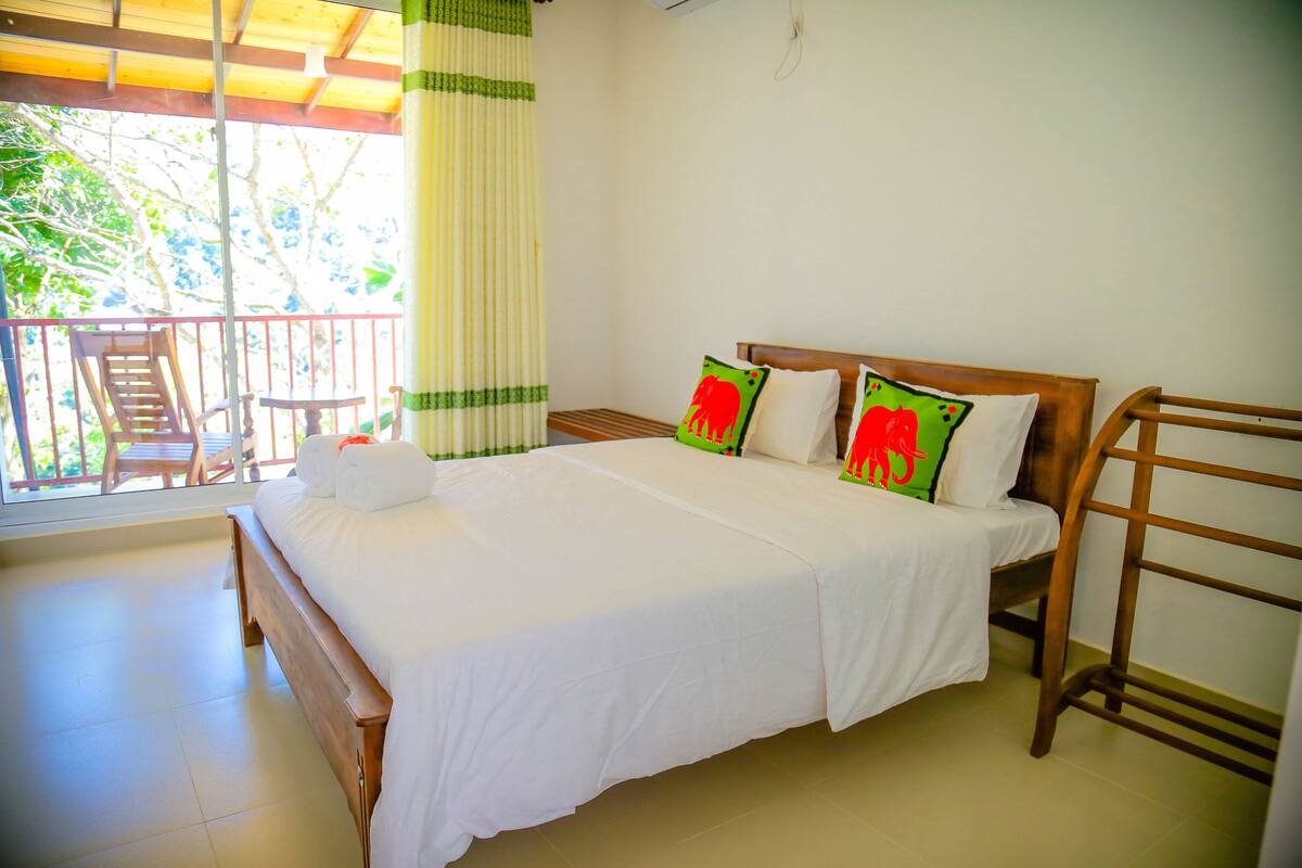 A neatly made bed with white linens and two pillows, a wooden headboard, and a balcony with a chair and table.