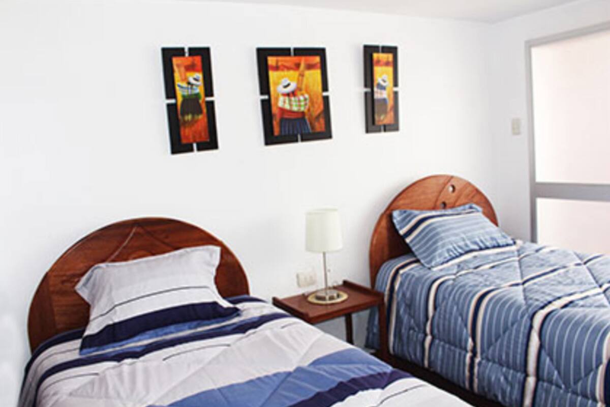 A bedroom with a wooden headboard bed, a smaller bed with a striped blanket, and three framed artworks on the wall.