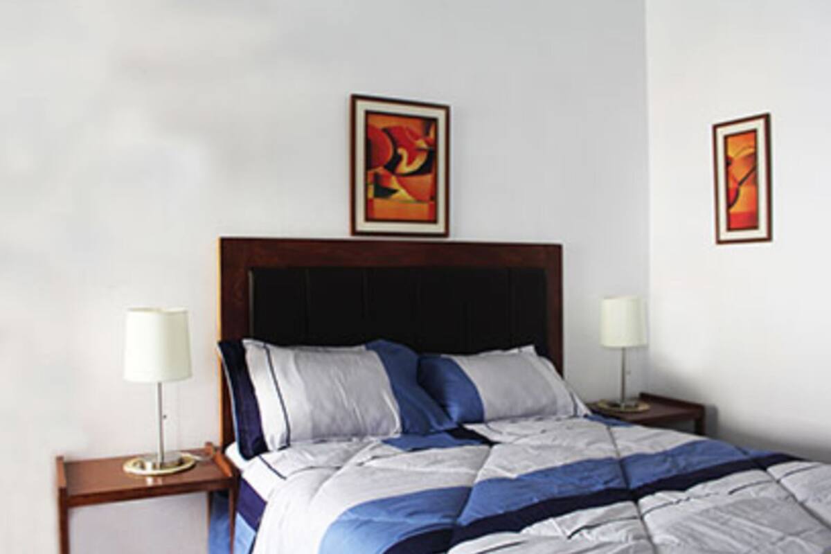 A hotel room with a large bed, two bedside tables with lamps, and two framed artworks on the wall.