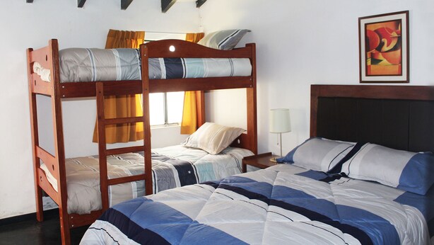 Een kamer met twee stapelbedden, een enkel bed, een nachtkastje en een ingelijst schilderij aan de muur.