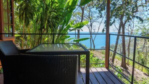 A covered outdoor seating area with a table and chairs, overlooking a scenic view of the sea and surrounding greenery. - Montezuma Heights "Geco" studio. In between ocean and the wild. Sleeps 2 (Montezuma)