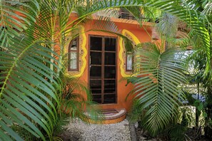 Un petit bâtiment coloré, doté d’une porte centrale et entouré d’une végétation luxuriante.