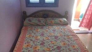 Cama com roupa de cama floral, cabeceira de madeira e janela com persianas.