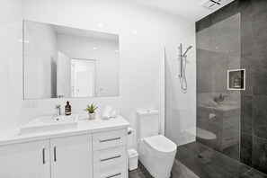 Een moderne badkamer met een grote spiegel, een witte wastafel, toilet en een douchecabine met glazen wanden.