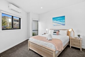 Een slaapkamer met een bed, nachtkastjes, een wandairconditioner, een raam met uitzicht en een schilderij aan de muur.