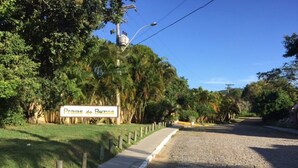 A paved road with a sign reading "Praias de Bahia" and a sidewalk with wooden posts. - Casa 4 suites a 200m da Rua das Pedras (Búzios)
