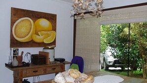 A dining area with a wooden table, a chandelier, and a large fruit painting on the wall. - Casa 4 suites a 200m da Rua das Pedras (Búzios)