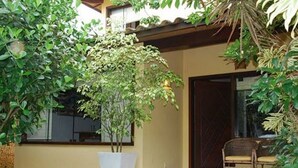 A house with a covered patio, a large potted plant, and a wicker chair. - Casa 4 suites a 200m da Rua das Pedras (Búzios)