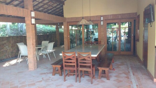 An outdoor dining area with a long table and chairs, a covered roof, and a view of the outdoors. - Casa 4 suites a 200m da Rua das Pedras (Búzios)