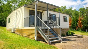 A single-story mobile home with a covered porch, a staircase, and a small patio area. - High View Accommodations # 3 (Freemans Reach)