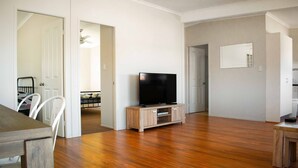 A spacious living room with hardwood flooring, a flat-screen TV on a wooden stand, and a dining area with a table and chairs. - High View Accommodations # 3 (Freemans Reach)
