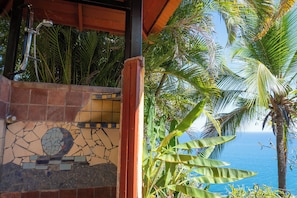 Ein gefliester Duschbereich mit Blick auf das Meer und Palmen.