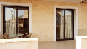 A balcony with a glass door, a wicker chair, and a small table. - Kyklades Resort DPSBF04 -Colorful One Bed Apartment- WIFI-Communal Pool-Gym-Spa (Pralimni)