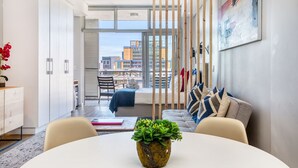 Una sala de estar moderna con una mesa redonda, un sofá y vistas de la ciudad a través de amplios ventanales.