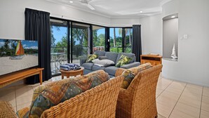 Ein modernes Wohnzimmer mit einem grauen Sofa, Korbmöbeln und einem Fernseher.