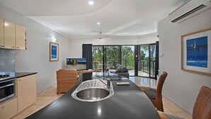 Eine moderne Küche mit einer zentralen Kochinsel, einem Essbereich mit Stühlen und einer großen Schiebeglastür, die auf einen Balkon mit Meerblick führt.