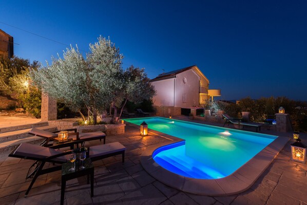 Relax by the serene pool surrounded by a patio and a majestic olive tree.