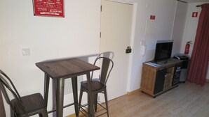 Une petite cuisine équipée avec une table en bois et des chaises en métal, un téléviseur et un coin bar agrémenté d’un panneau indiquant les règles à respecter dans la cuisine.