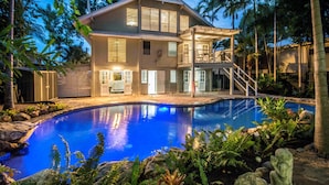Una casa de dos pisos con piscina, rodeada de vegetación tropical.