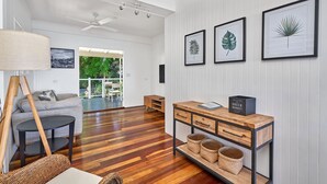 Un salón amplio con piso de madera, un sofá, una mesa de centro, una lámpara, un televisor y obras de arte enmarcadas en la pared.